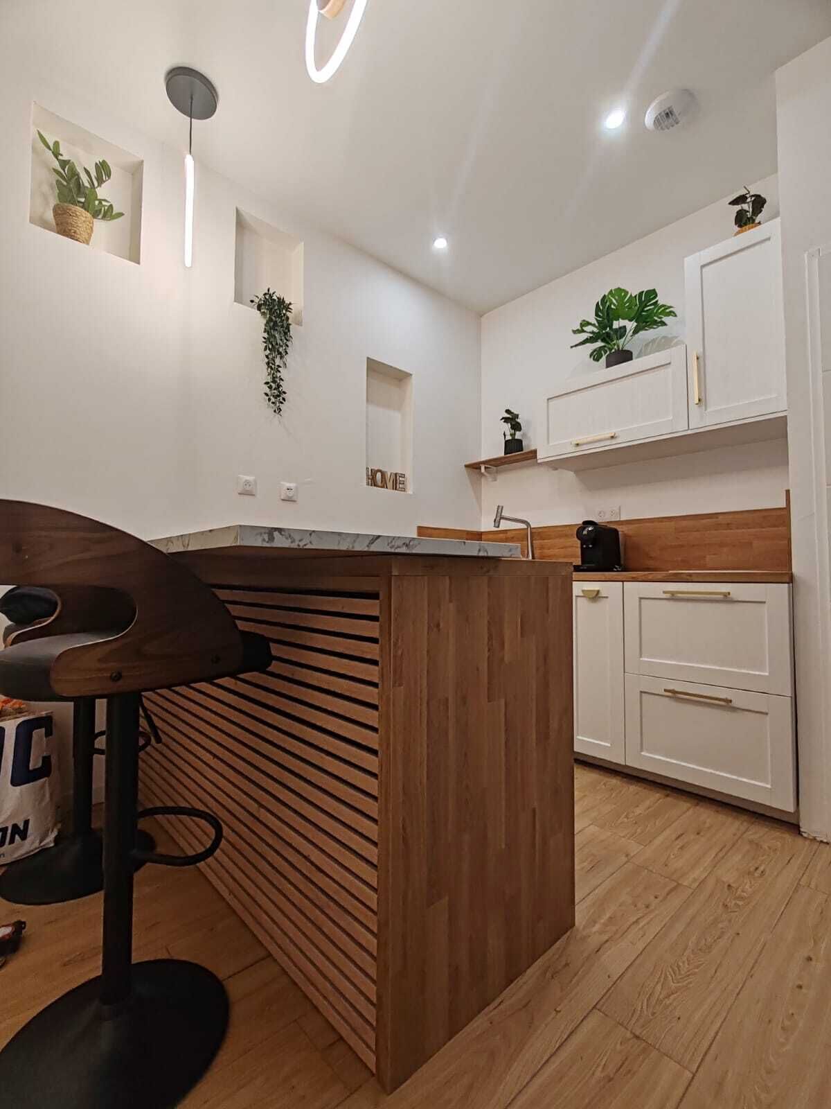 A modern kitchen with a wooden island, white cabinetry, and built-in plants.