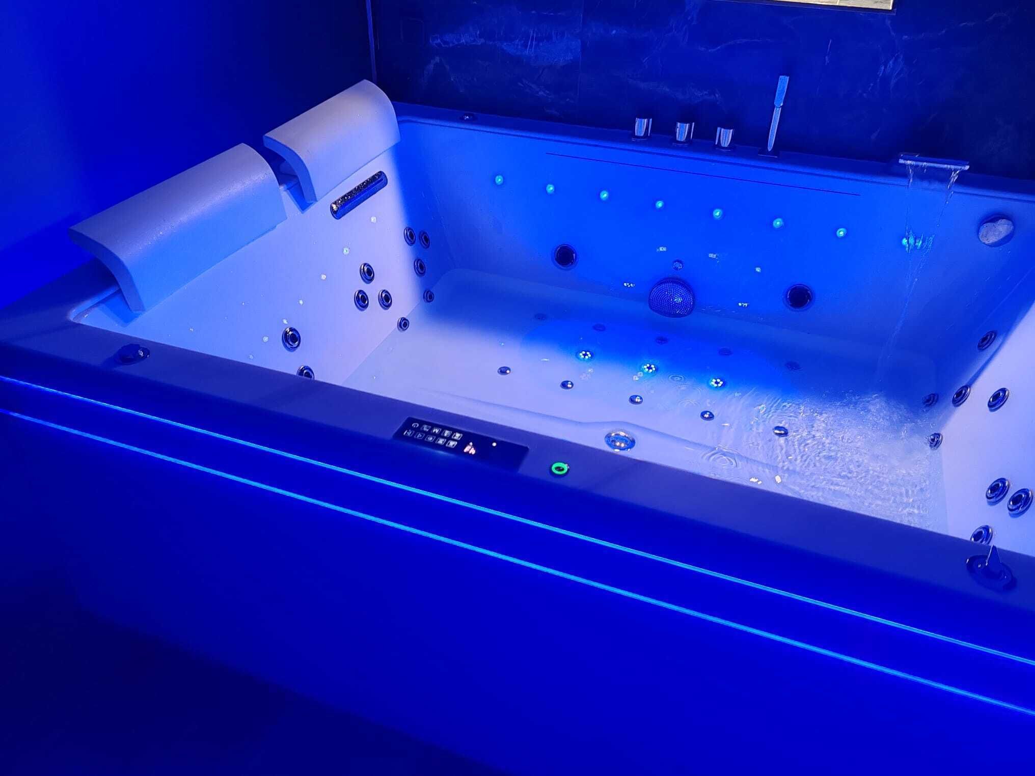 A modern spa tub with multiple jets, a control panel, and LED lighting.