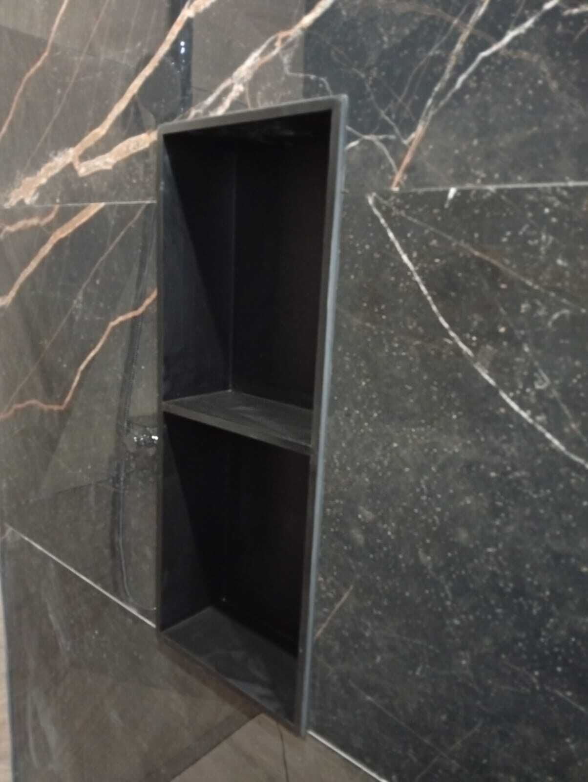 Un coin de pièce avec un mur en marbre foncé et une étagère en métal noir.