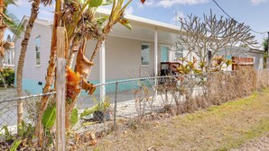 A single-story house with a porch, a fenced yard, and a banana tree in the foreground. - Fork River Getaway in Stuart: 6 Mi to Downtown! (Stuart)