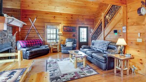 Un acogedor interior de cabaña de madera con chimenea, sofás de cuero, una escalera de madera y decoración rústica.