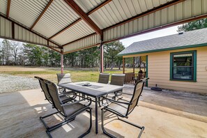 An outdoor covered patio with a table and chairs, a small building with a window, and a grassy area with trees in the background. - Private 60-Acre Retreat Near Lake Murray & Texoma (Marietta)