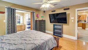A bedroom with a bed, a ceiling fan, a TV, and a view into the kitchen. - Explore Gulf Coast & Beyond! Home w/ Yard & Games (Long Beach)