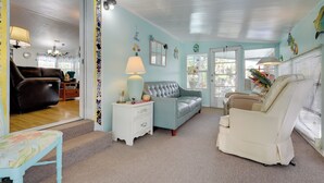 A cozy living room with a blue sofa, a white armchair, and a small table with a lamp. There is a staircase leading to another room.