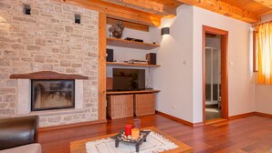 Ein gemütliches Wohnzimmer mit Kamin aus Stein, Holzbalken und einem Fernseher auf einer Holzregal.