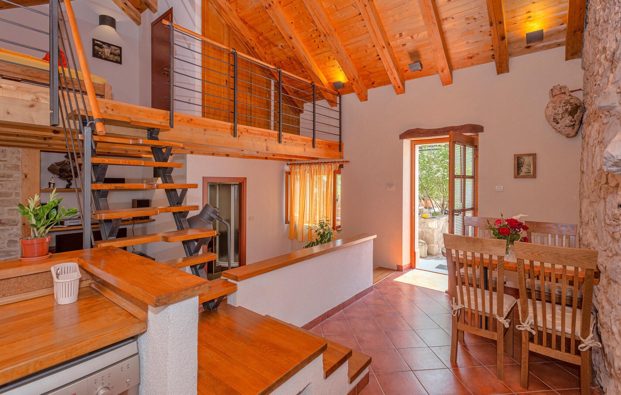 Um interior espaçoso com escada de madeira, área de jantar com mesa e cadeiras, e vista pela janela.
