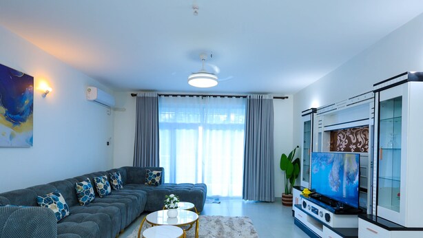 Ein modernes Wohnzimmer mit Sofa, zwei Couchtischen, Fernseher und Küchenzeile.