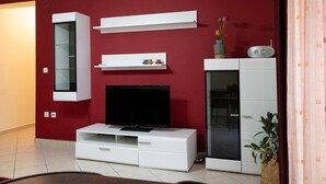 A modern living room with a red wall, white entertainment unit, and a television. - Cozy apartment in Sykies by MPS (Συκιές)