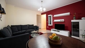 A modern living room with a black sofa, a glass coffee table, and a wooden bowl with fruits. - Cozy apartment in Sykies by MPS (Συκιές)