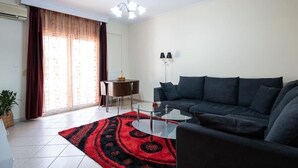 A living room with a dark sofa, a glass coffee table, a red and black rug, a dining table with chairs, and a chandelier. - Cozy apartment in Sykies by MPS (Συκιές)