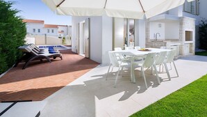 Een terras buiten met een eettafel en stoelen, een barbecue en een zwembad.