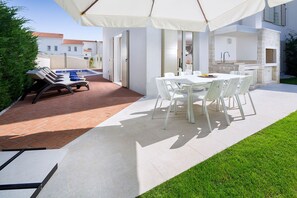 Eine Terrasse im Freien mit Esstisch und Stühlen, einem Grill und einem Swimmingpool.