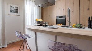 Een moderne keuken met houten kastjes, een roestvrijstalen afzuigkap en een ingebouwde oven. Er is een bar met een glazen stoel en een boek.