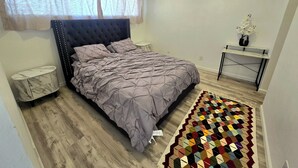 A bedroom with a bed, bedside tables, a nightstand, a small desk, a chair, a patterned rug, and a window with sheer curtains. - Cozy 1-bedroom apartment in Downtown beautiful San Diego with AC (San Diego)
