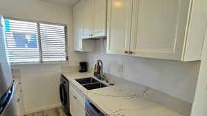 A compact kitchen with white cabinets, a built-in dishwasher, and a marble countertop. - Cozy 1-bedroom apartment in Downtown beautiful San Diego with AC (San Diego)