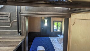 Una habitación pequeña y cerrada con una cama, un ventanal y una puerta que da a otra estancia.