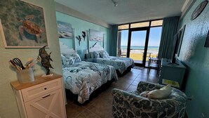 Una habitación con dos camas, un escritorio, una silla y vista al mar.