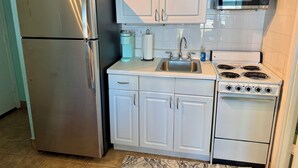 Cocina compacta con armarios blancos, un refrigerador de acero inoxidable, un microondas y una estufa.
