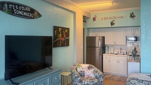Un espacio habitable compacto con televisión, sofá, zona de comedor pequeña y kitchenette.