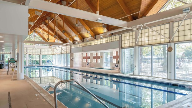 Piscina interior com vigas de madeira, janelas amplas e vista para o exterior.