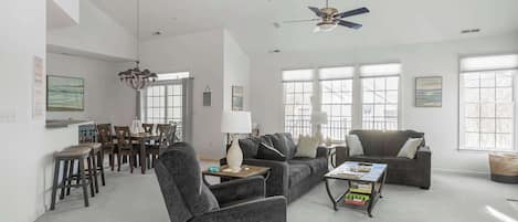 A spacious living room with a gray sofa, a coffee table, and a dining area with wooden chairs and a table.