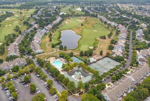 An aerial view of a residential area with houses, a golf course, a swimming pool, and tennis courts. - Bear Trap Glory Pools & Golf (Ocean View)