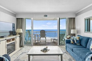Ein Zimmer mit Fernseher, einer Couch, einem Couchtisch und einem Balkon mit Meerblick.