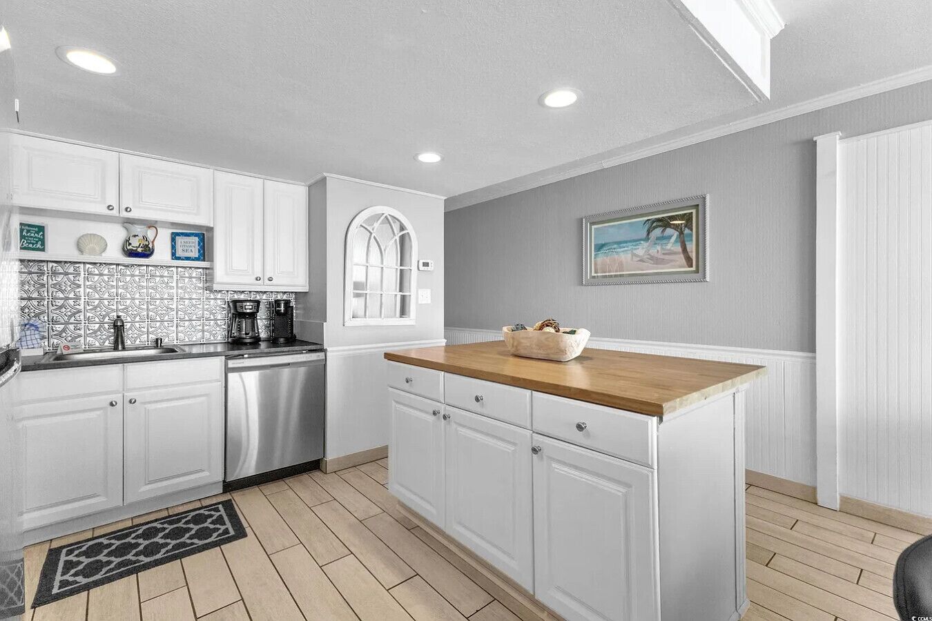 A modern kitchen with white cabinetry, a wooden countertop, and a tiled backsplash.