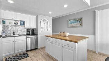 A modern kitchen with white cabinetry, a wooden countertop, and a tiled backsplash.