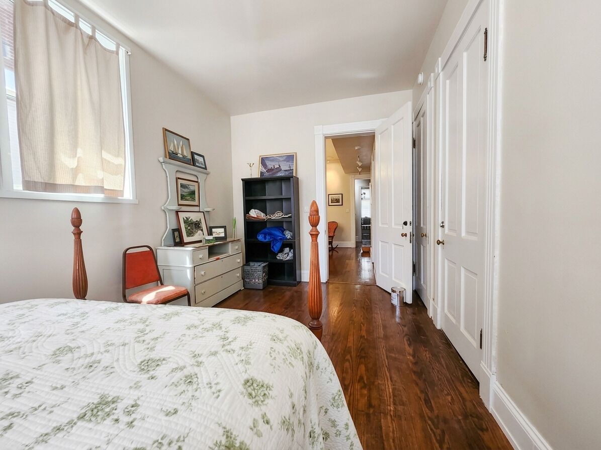A bedroom with a bed, a dresser, a chair, a bookshelf, and a door leading to another room.