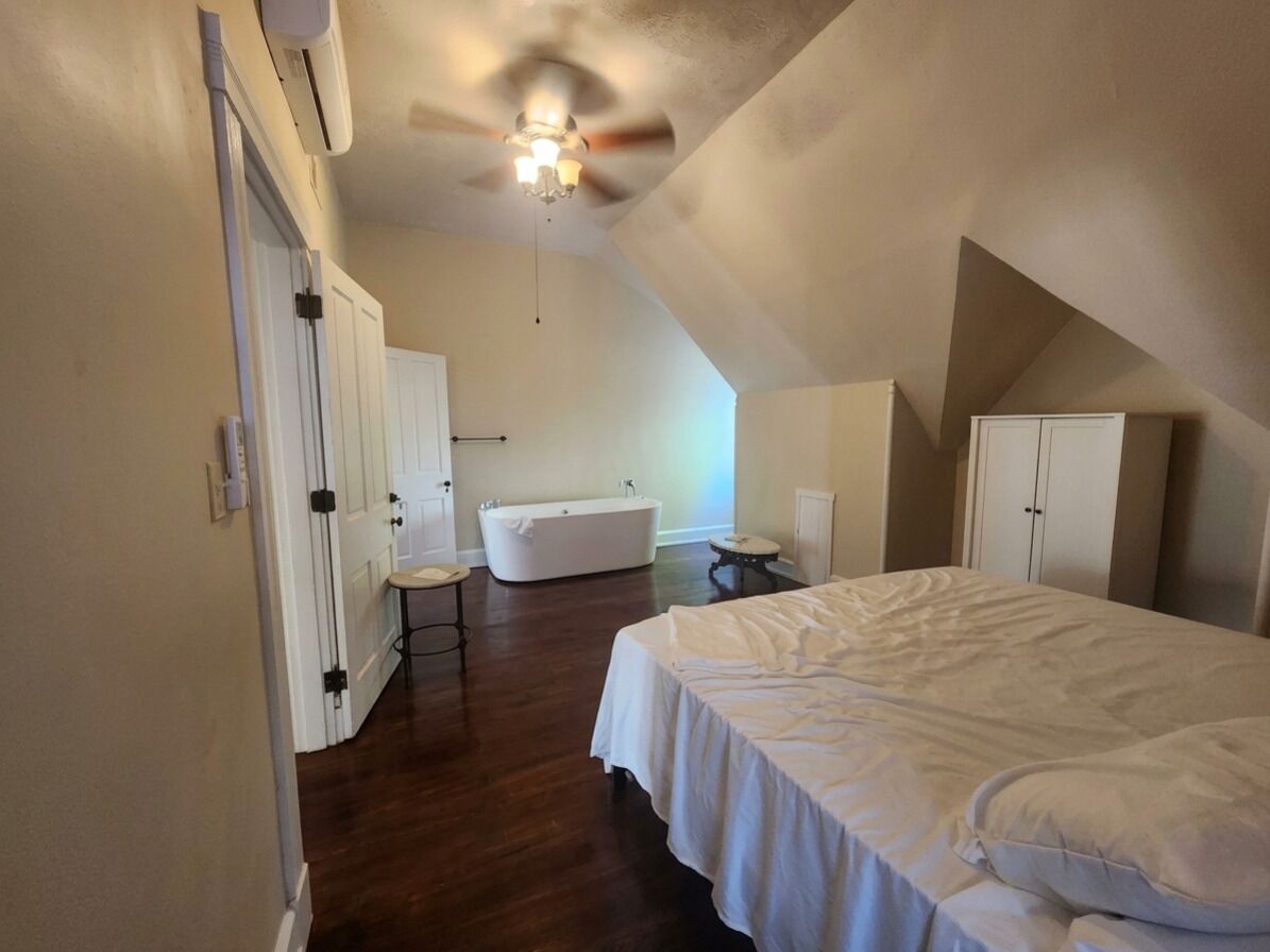 A bedroom with a bed, a ceiling fan, a bathtub, and a wardrobe.
