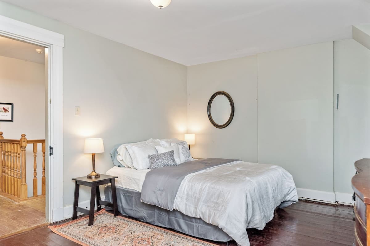 Un dormitorio con una cama, dos lámparas de noche, un espejo y una alfombra estampada.