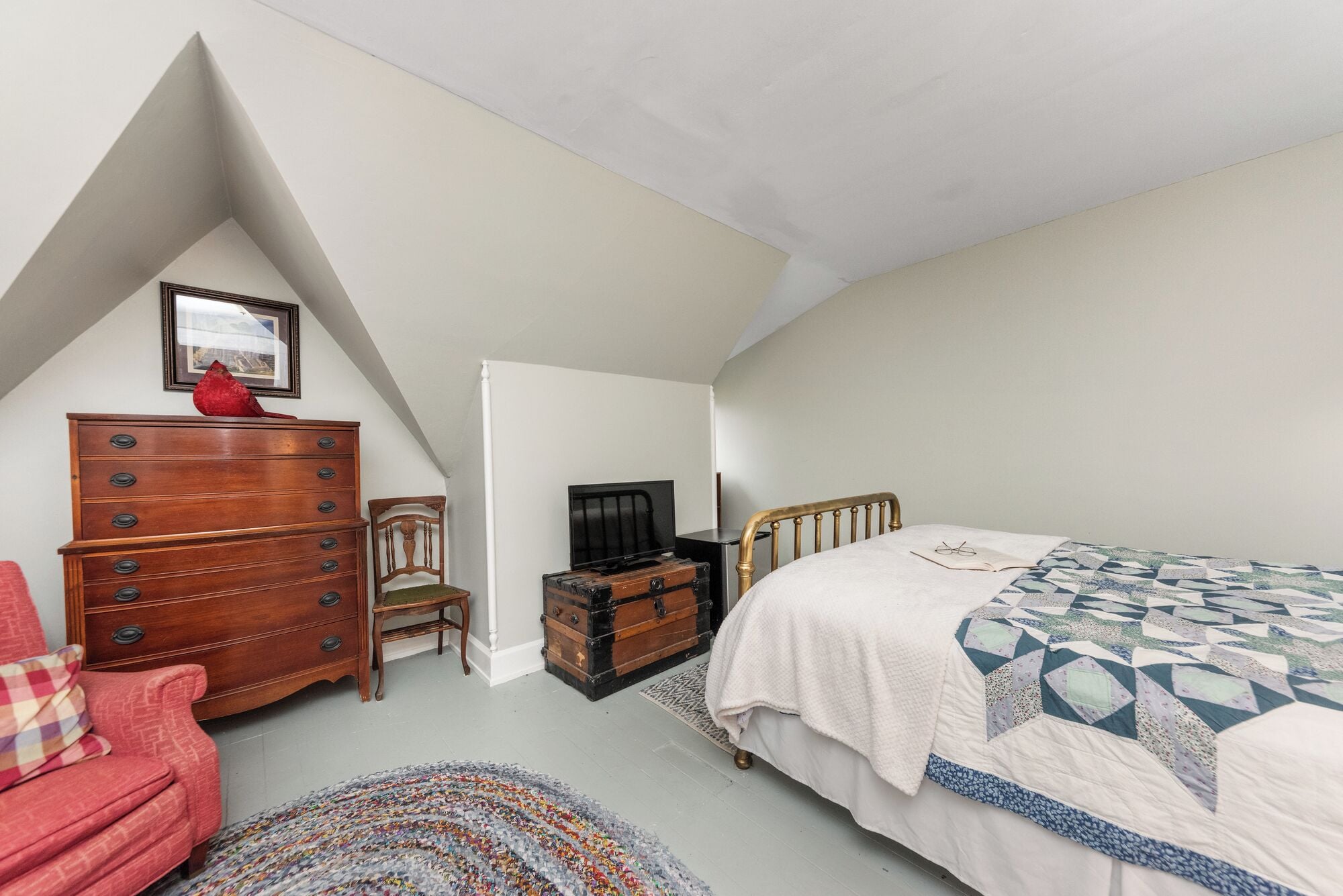 Ein Schlafzimmer mit Bett, Kommode, Stuhl und Fernseher.