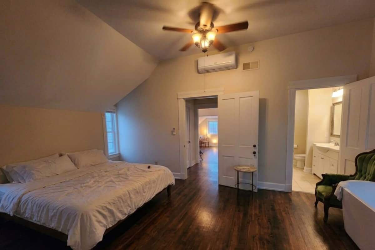 Un dormitorio con cama, ventilador de techo y puerta que da a un baño.