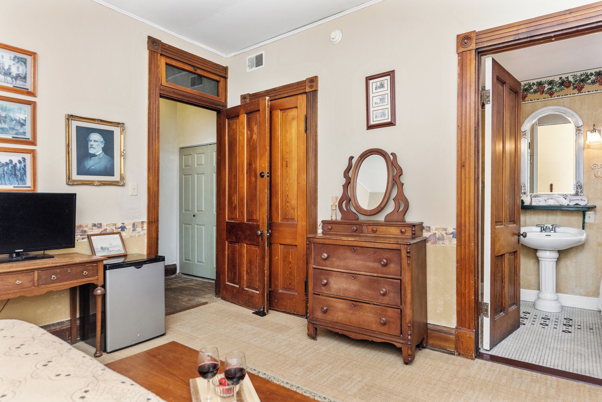 Ein Zimmer mit einem Holzkasten, einem Fernseher, einem Spiegel und einer Tür zu einem weiteren Raum.