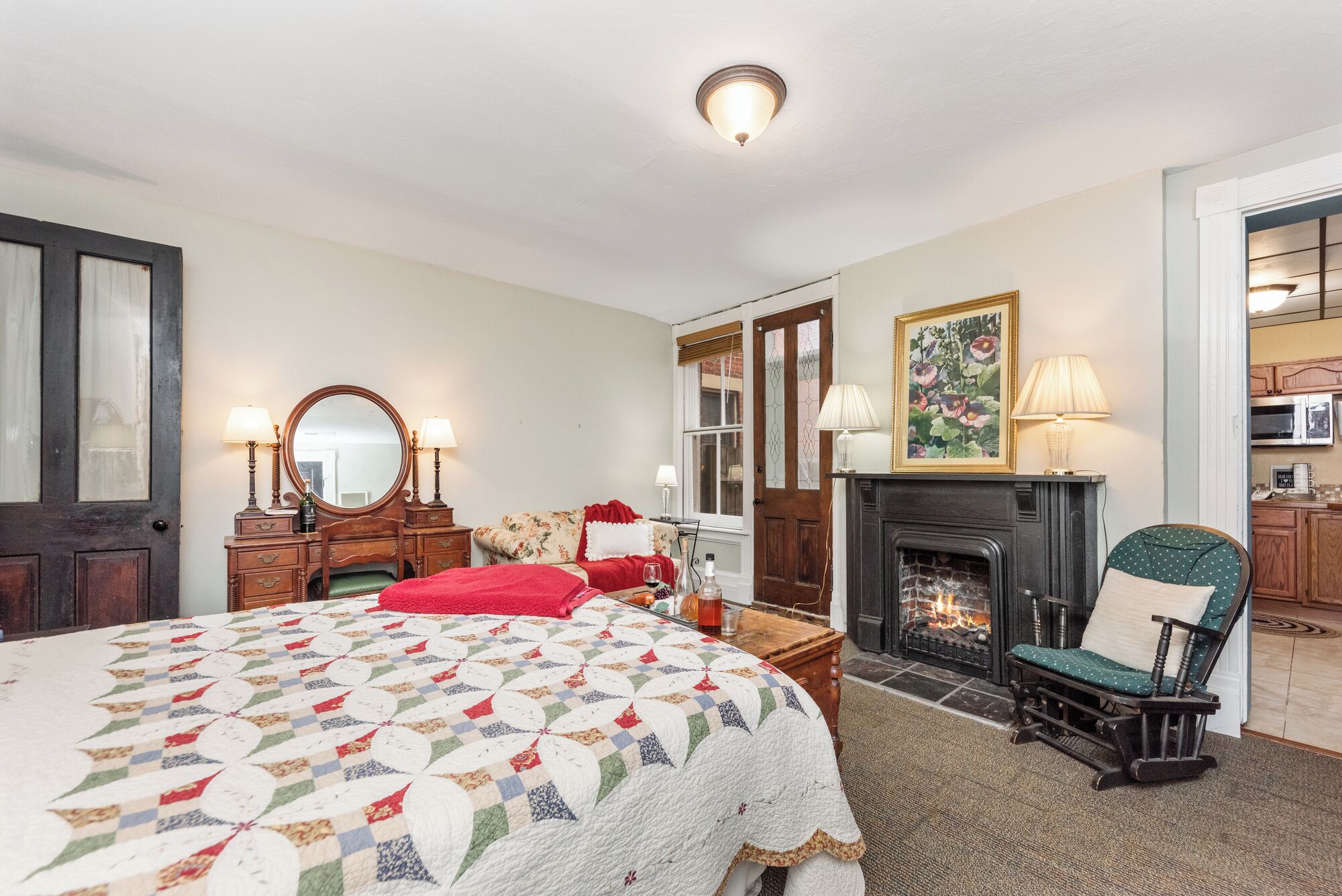 Une chambre à coucher avec un grand lit, une cheminée, un fauteuil, une commode et un miroir.