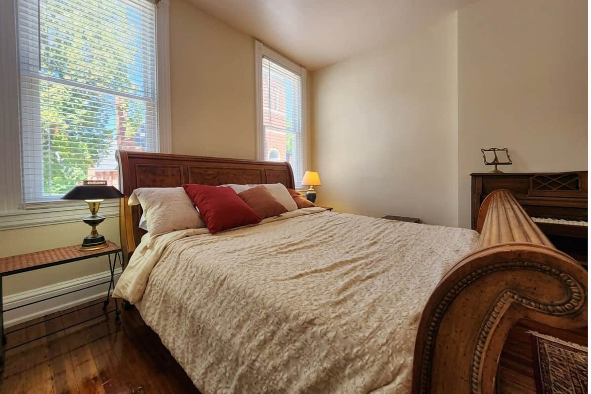 Un dormitorio con cama, mesita de noche, lámpara, piano y ventana con persianas.