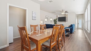 A dining area with a wooden table and chairs, a ceiling fan, and a TV mounted on the wall. - Home Away from Home (Fort Worth)