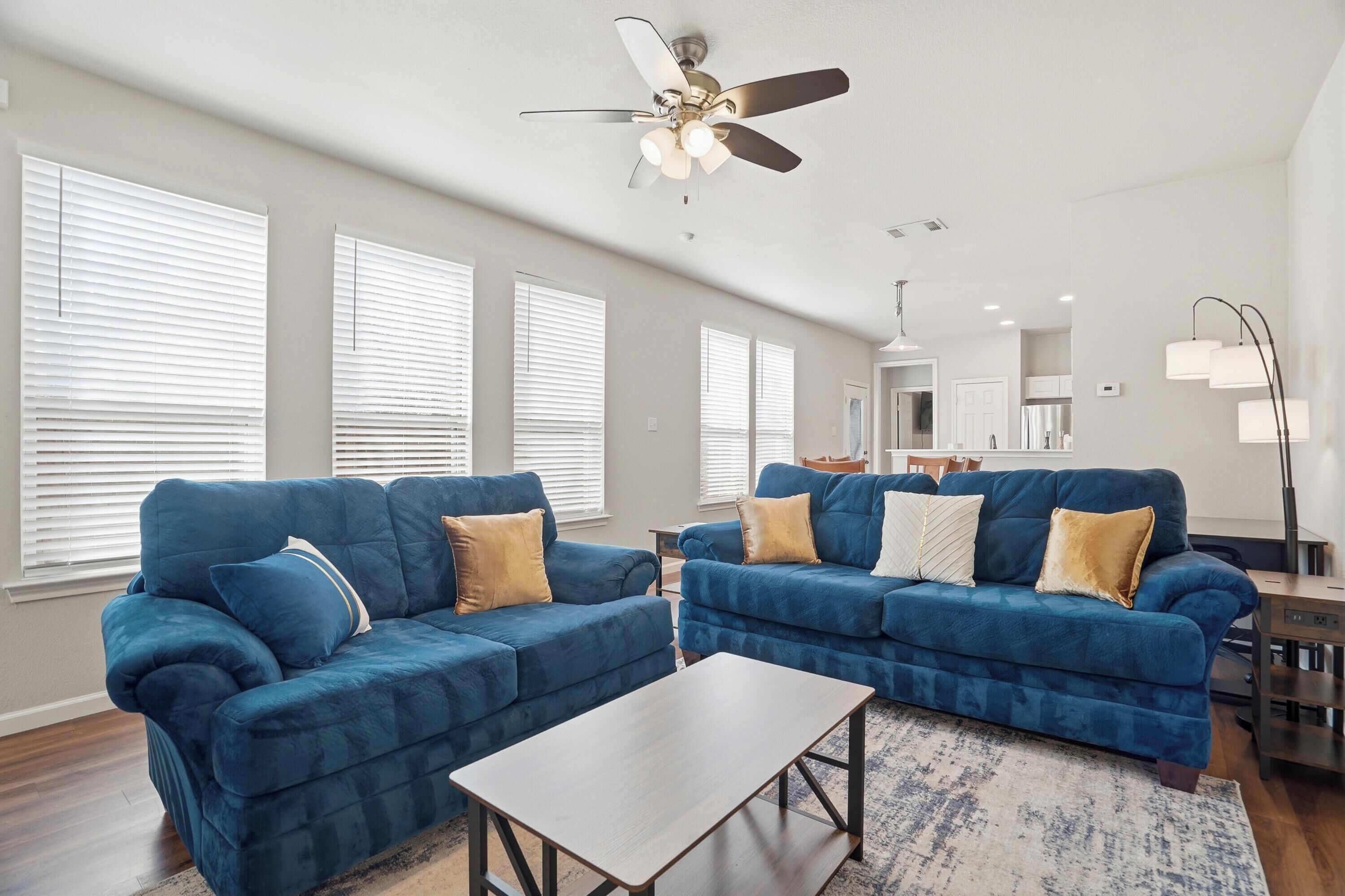 Ein Wohnzimmer mit zwei blauen Sofas, einem Couchtisch und einem Deckenventilator.