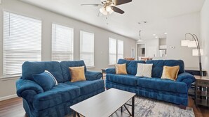 A living room with two blue sofas, a coffee table, and a ceiling fan. - Home Away from Home (Fort Worth)