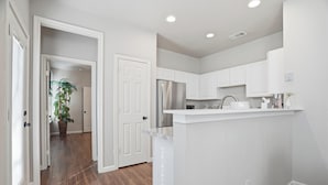 A modern kitchen with white cabinetry, a stainless steel refrigerator, and a countertop with a sink. - Home Away from Home (Fort Worth)