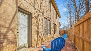 A brick building with a wooden fence, a door with a shutter, and a blue chair on a paved walkway. - Home Away from Home (Fort Worth)
