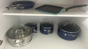 En køkkenhylde med kogegrej, heriblandt en stegepande, et bagefad og flere gryder.
