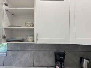 Une cuisine avec des meubles blancs, un dosseret carrelé et une machine à café posée sur le plan de travail.