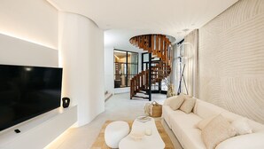 Uma sala de estar moderna com televisão de tela plana, um sofá branco, uma mesa de centro diferenciada e uma escada com corrimão de madeira.