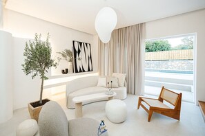 A modern living room with a white sofa, a wooden chair, a potted plant, and a large window with curtains.