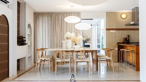 Uma sala de jantar moderna com uma mesa branca, seis cadeiras de madeira e um vaso de flores.