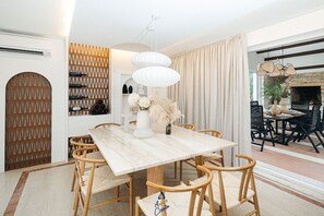 A dining area with a marble table, wicker chairs, a white pendant light, and a view of an outdoor patio with a fireplace.