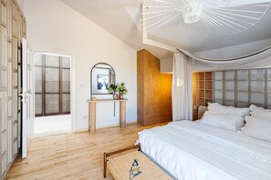 A modern bedroom with a large bed, a wooden floor, a mirror, a small table with a vase, and a unique ceiling light fixture.
