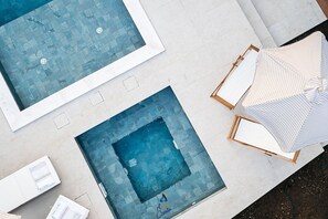 Two swimming pools with tiled floors and a lounge area with striped umbrellas.
